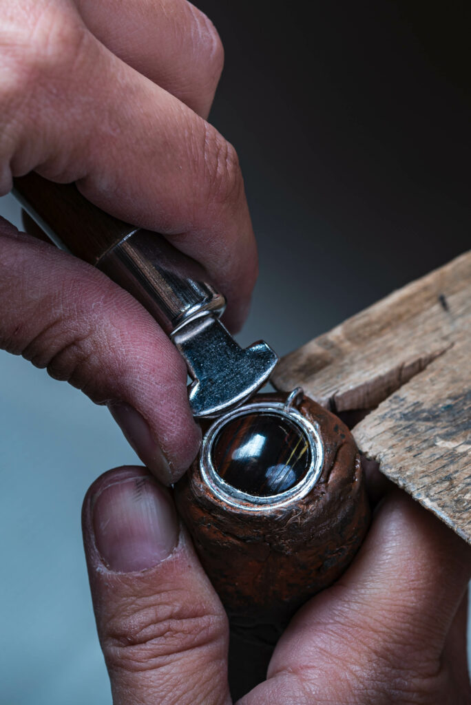 jeweller setting a tiger iron stone into the bezel set on the si